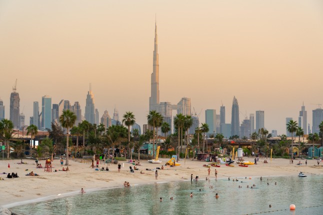 Foto matahari terbenam Dubai dengan pantai dan gedung pencakar langit.