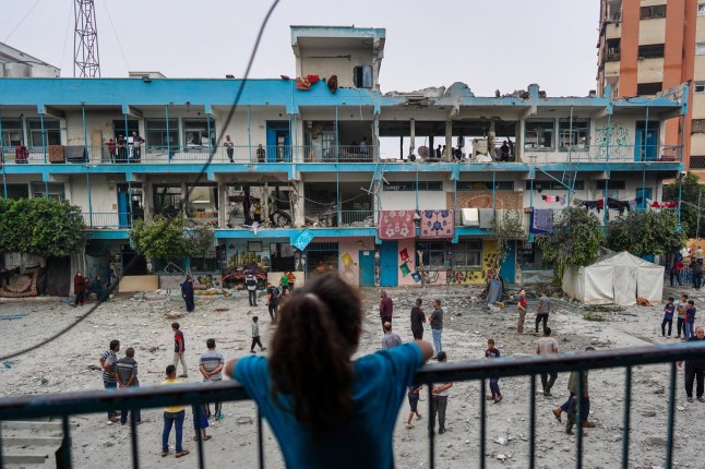 Seorang gadis Palestina menyaksikan orang lain memeriksa akomodasi sekolah PBB memindahkan orang-orang yang terkena serangan bom Israel di Nuseirat, Jalur Gaza tengah, 6 Juni 2024, di tengah konflik antara Israel dan kelompok militan Palestina Hamas. Militer Israel mengatakan pada tanggal 6 Juni bahwa pesawat tempurnya telah menyerang sebuah sekolah milik PBB yang digunakan oleh militan Palestina di Gaza tengah, dan pihak berwenang di wilayah yang dikuasai Hamas melaporkan sedikitnya 27 orang tewas. (Foto oleh Bashar TALEB / AFP) (Foto oleh BASHAR TALEB/AFP via Getty Images)