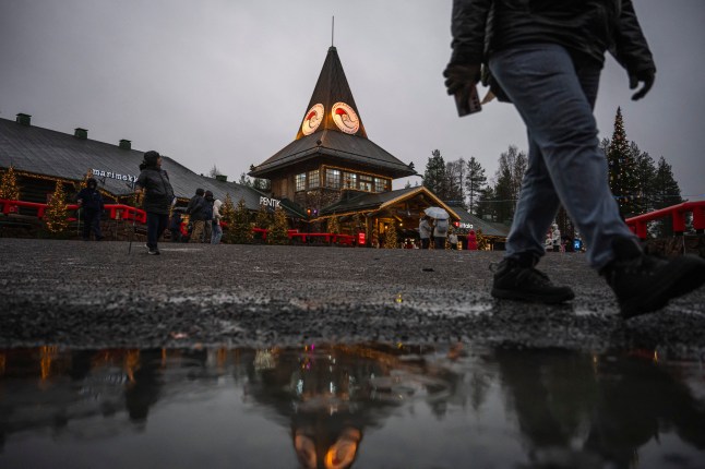Seorang turis berjalan di atas genangan air hujan saat berkunjung ke Desa Santa Claus dekat Rovaniemi, Lapland Finlandia, 16 November 2024. Menjelang Natal satu bulan lagi, Sinterklas sedang sibuk mempersiapkan diri, namun pemanasan global dan minimnya salju di kampung halamannya membuat Arktik membuatnya khawatir. Pada saat ini, kota Rovaniemi, di Lapland Finlandia, disebut-sebut oleh pejabat pariwisata sejak tahun 1980an sebagai "nyata" Rumah Santa - harus berwarna putih dan cantik. (Foto oleh Jonathan NACKSTRAND / AFP) (Foto oleh JONATHAN NACKSTRAND/AFP via Getty Images)