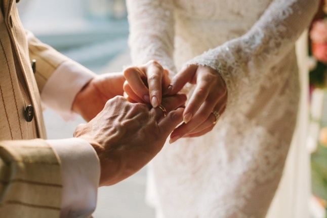 Pengantin wanita memasangkan cincin di jari pengantin pria. Pertukaran cincin. Pasangan bahagia merayakan pernikahan di luar ruangan di musim panas.