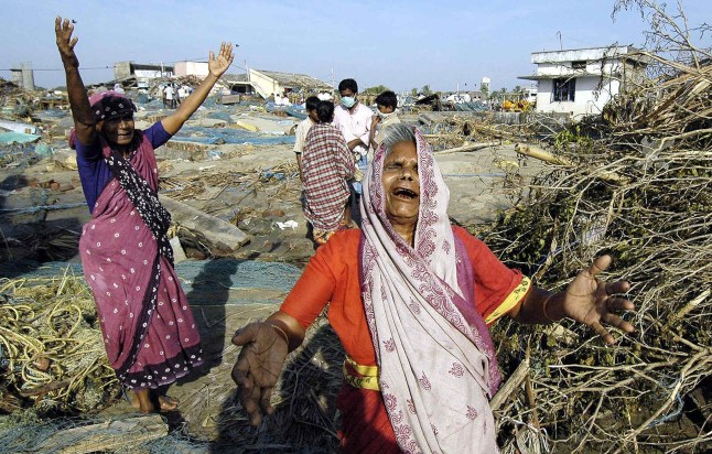 TOPSHOT - Wanita India menangis saat melihat rumah mereka hancur di koloni nelayan tepi laut Akarapatti dekat pelabuhan Nagapattinam, sekitar 350 km selatan Madras, 30 Desember 2004, setelah gelombang pasang melanda wilayah tersebut. Birokrasi India yang rumit tidak memberikan peringatan dini mengenai tsunami, sehingga menyia-nyiakan waktu berharga yang sebenarnya bisa menyelamatkan nyawa, demikian yang dilaporkan surat kabar pada tanggal 30 Desember. Angkatan Udara India diperingatkan bahwa sebuah pangkalan terpencil di pulau Car Nicobar telah terendam banjir jauh sebelum gelombang raksasa menghantam pantai daratan ratusan mil jauhnya pada pagi hari tanggal 26 Desember, kata Indian Express. AFP PHOTO/Prakash SINGH (Foto oleh PRAKASH SINGH / AFP) (Foto oleh PRAKASH SINGH/AFP via Getty Images)