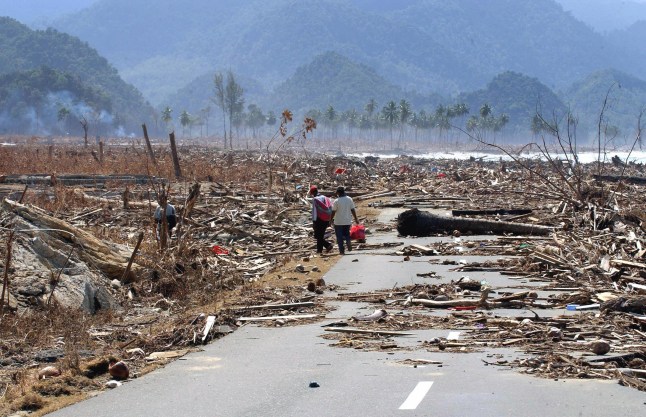 LEUPUNG, INDONESIA: Dua pengungsi Indonesia berjalan di jalan yang tertutup puing-puing akibat bencana tsunami saat mereka kembali ke rumah mereka di kota pantai barat Leupung, sekitar 30 km dari Banda Aceh, pada tanggal 9 Januari 2005. Kekhawatiran masih ada hingga tanggal 9 Januari bahwa sejumlah korban selamat tsunami di provinsi Aceh, Indonesia, belum menerima bantuan apa pun, dua minggu setelah bencana tersebut memakan korban jiwa lebih dari 104.000 orang di negara ini. AFP PHOTO/CHOO YOUN-KONG (Kredit foto harus dibaca CHOO YOUN-KONG/AFP via Getty Images)