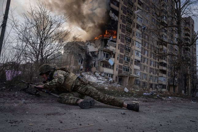 FILE - Seorang petugas polisi Ukraina berlindung di depan gedung yang terbakar akibat serangan udara Rusia di Avdiivka, Ukraina, Jumat, 17 Maret 2023. (AP Photo/Evgeniy Maloletka, File)