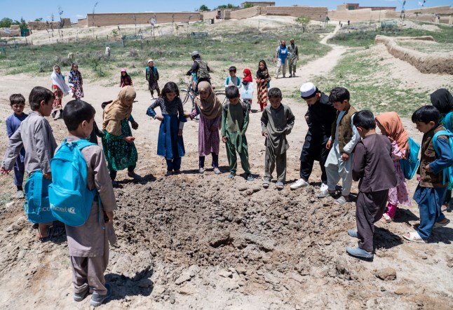 Dalam foto yang diambil pada 14 Mei 2024 ini, anak-anak berkumpul di sekitar kawah setelah penjinak ranjau Afghanistan dari Halo Trust meledakkan ranjau anti-tank di desa Qach Qala, provinsi Ghazni. Jamur hitam baru saja hilang di provinsi Ghazni ketika anak-anak berkumpul di tepi kawah yang diciptakan oleh tambang, salah satu alat yang membunuh seorang anak setiap dua hari di Afghanistan. (Foto oleh Wakil KOHSAR / AFP) / Untuk menyertai laporan AFP tentang anak-anak yang kecelakaan ranjau di Afghanistan, LAPORAN oleh Qubad Wali dan Pascale Trouillaud (Foto oleh WAKIL KOHSAR/AFP via Getty Images)